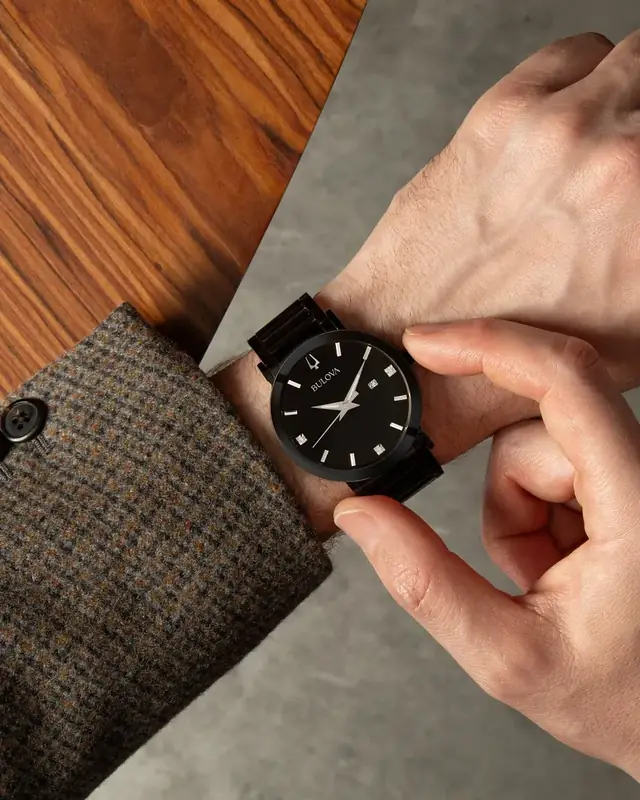 Reloj Bulova clásico negro con malla de acero negra en la muñeca de un hombre de saco